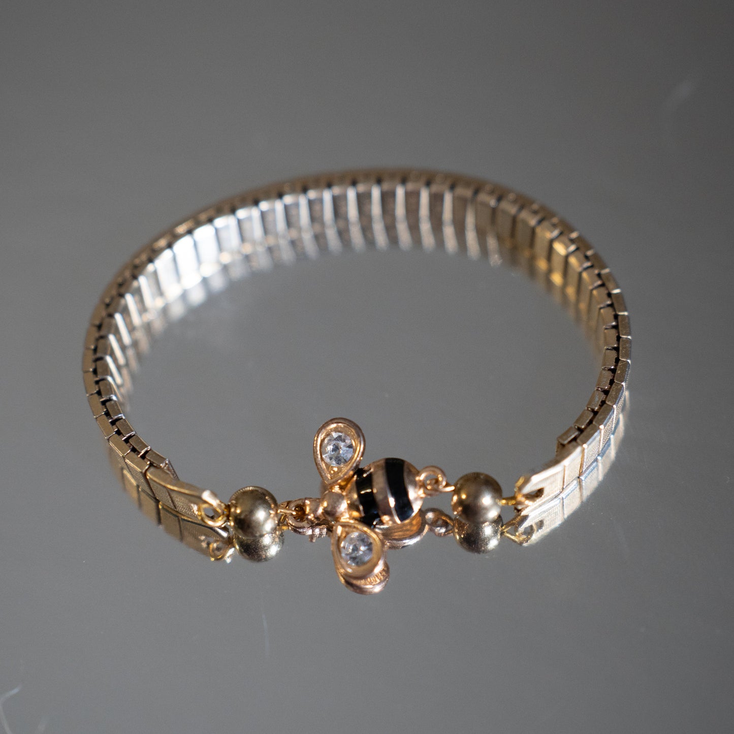 Gold bracelet with decorative bee elements on a gray background