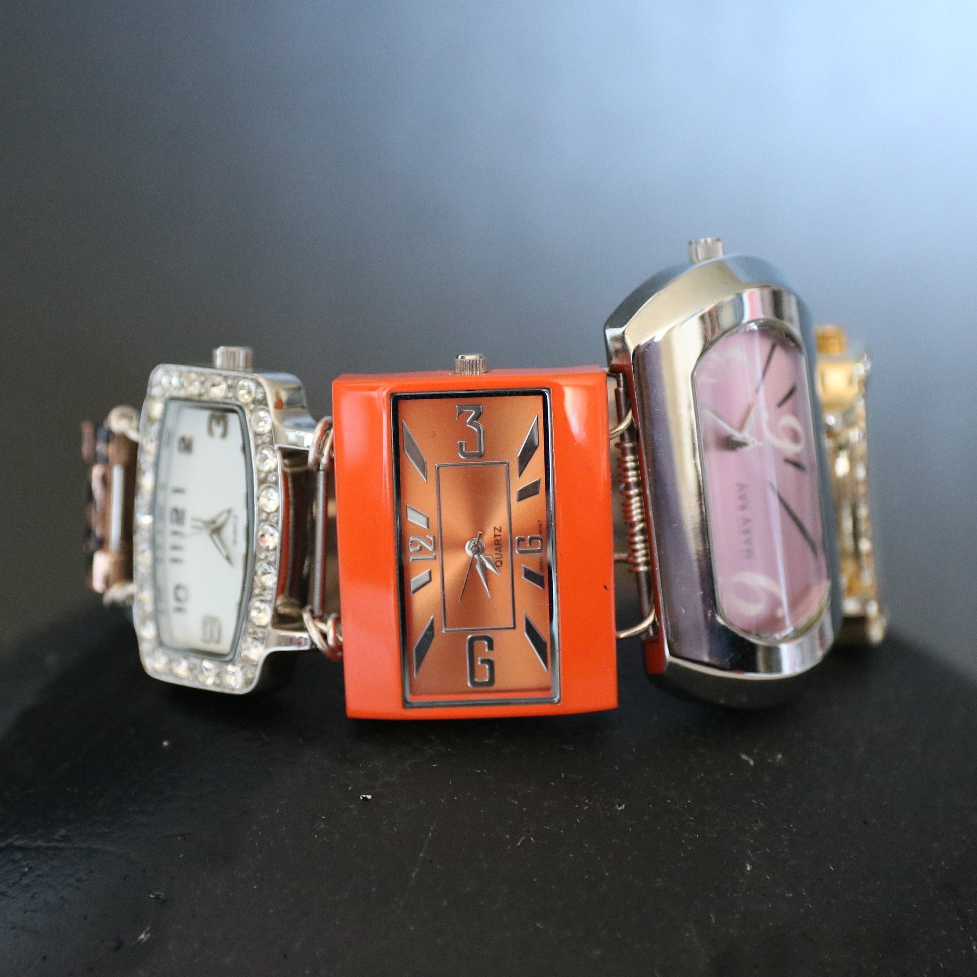 Three decorative watches on a black surface with a dark background